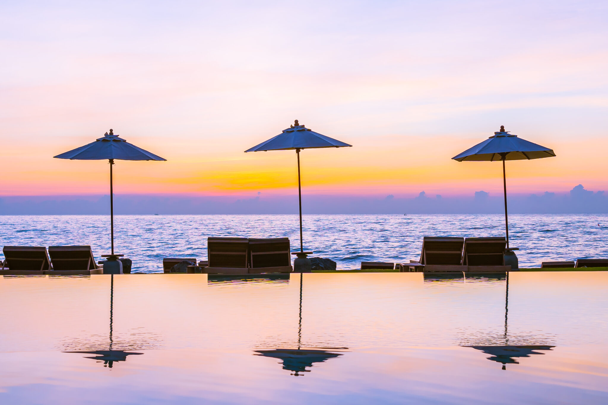 Umbrella and chair around swimming pool in resort hotel for leisure travel and vacation neary sea ocean beach at sunset or sunrise time